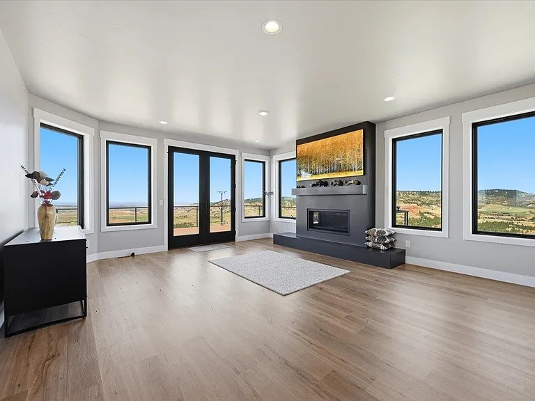 A curved wall of windows wraps around a living room with a dark fireplace and an aspen-grove canvas above the mantel.