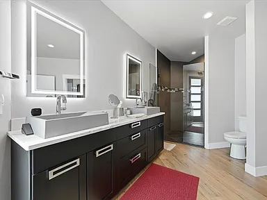 A dark double vanity with backlit mirrors sits opposite a glass-enclosed shower