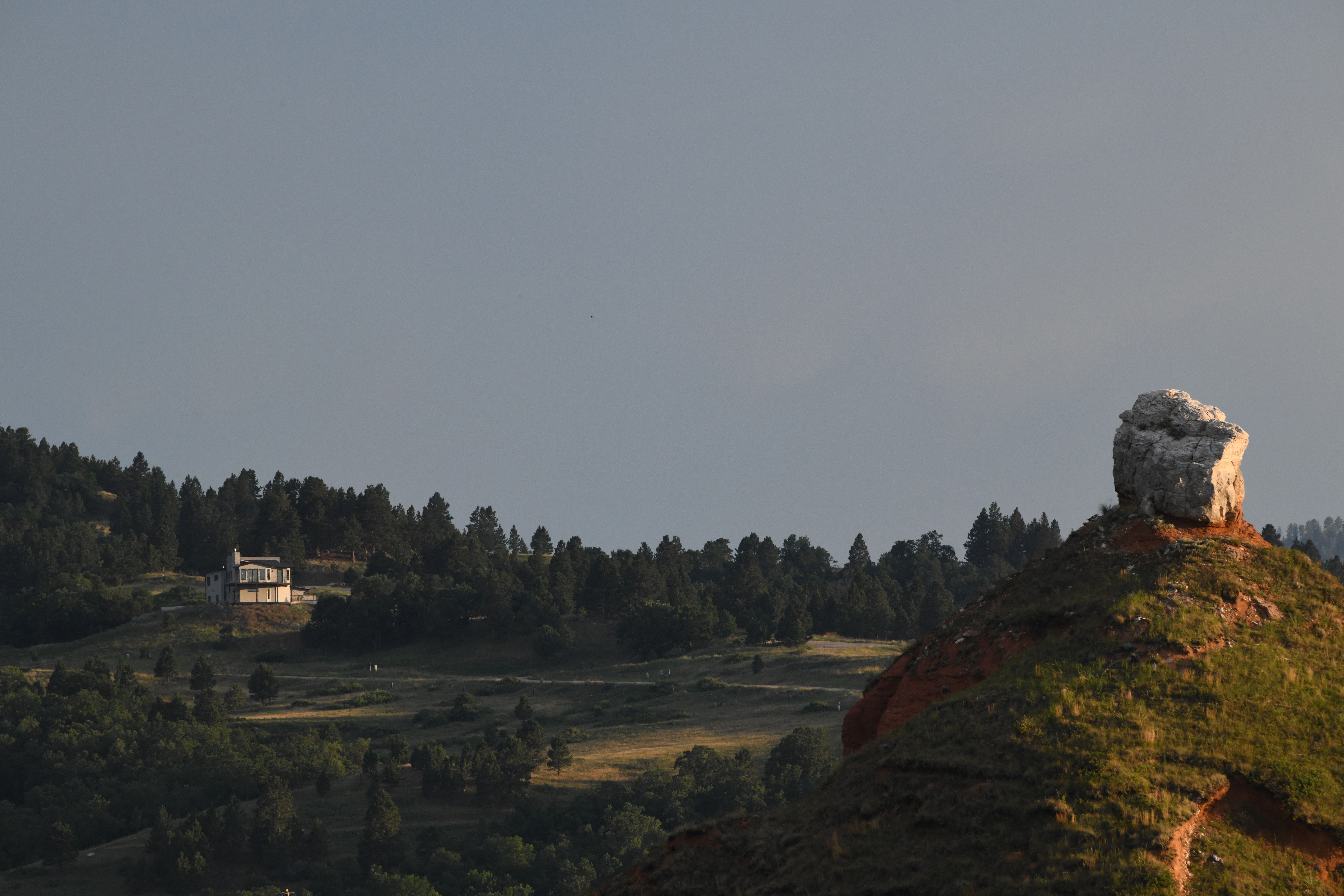 The house is visible in the distance across a wooded valley