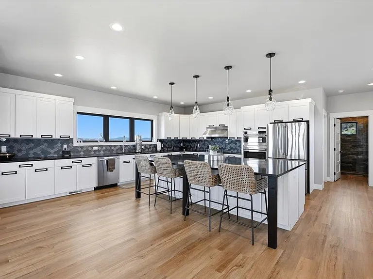 The kitchen features a black-topped island with glass pendant lights