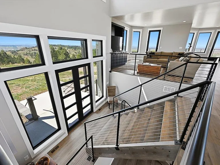 Cable-railed stairs descend past floor-to-ceiling windows toward an open living room with a sectional sofa at 2111 Vantage Circle.