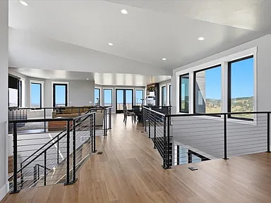 An upper hallway with cable railing overlooks the living and dining areas below