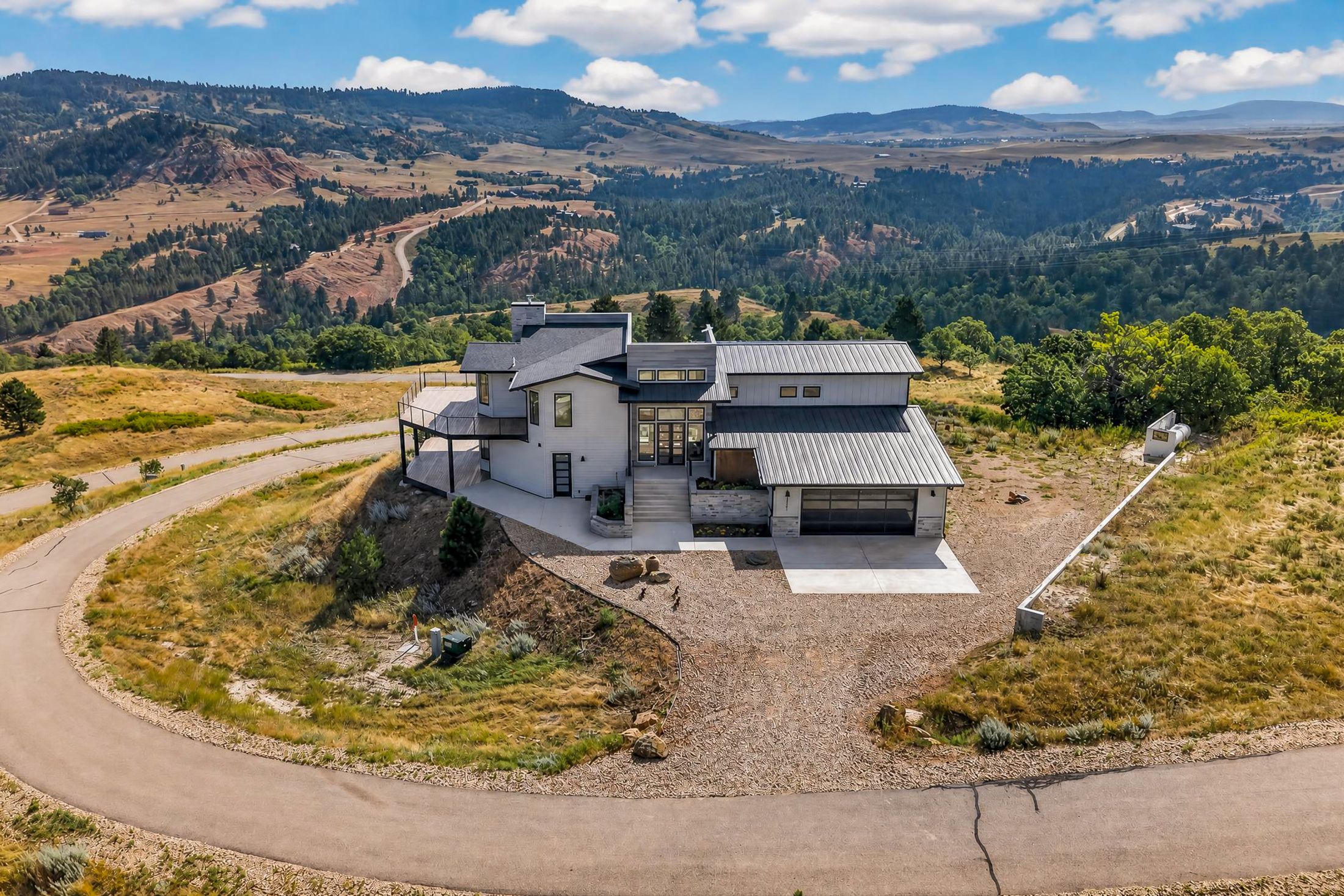 The property is shown from above with a red-toned eroded hillside and winding gravel road visible in the middle distance.