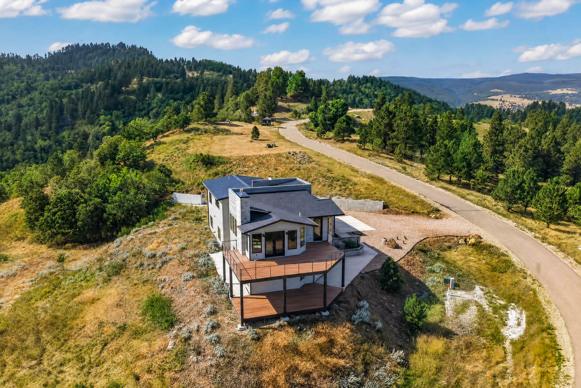 An aerial view shows the rear of 2111 Vantage Circle with its stone-walled terrace and covered lower deck set against the winding driveway.