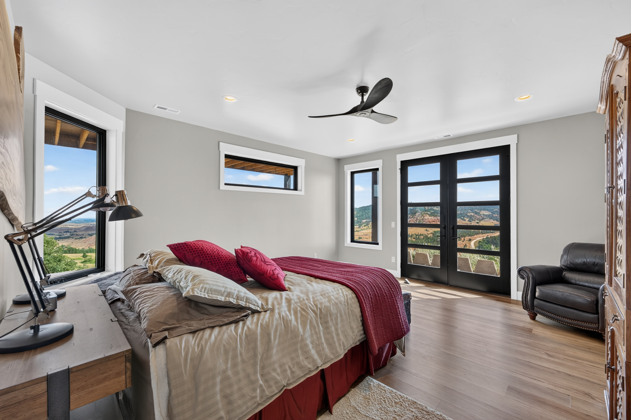 A guest bedroom with red and taupe bedding opens through glass doors onto a small balcony over the valley.