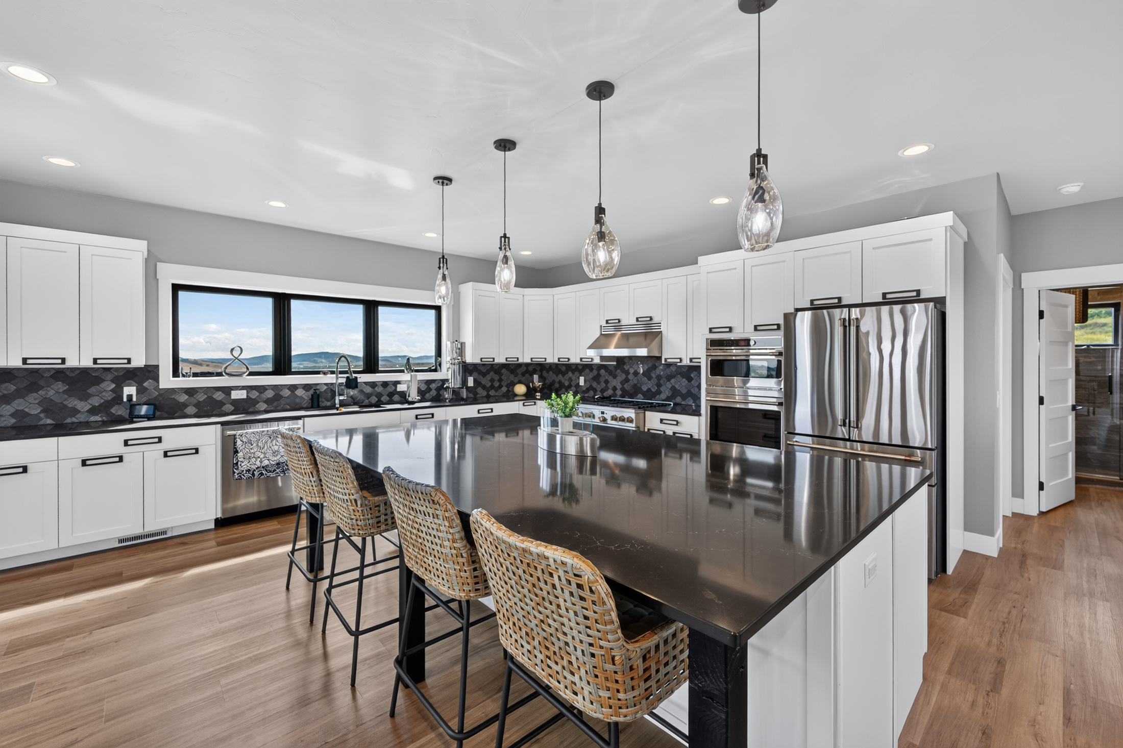 A black quartz island anchors the kitchen, with woven counter stools and a view toward the range and double ovens.