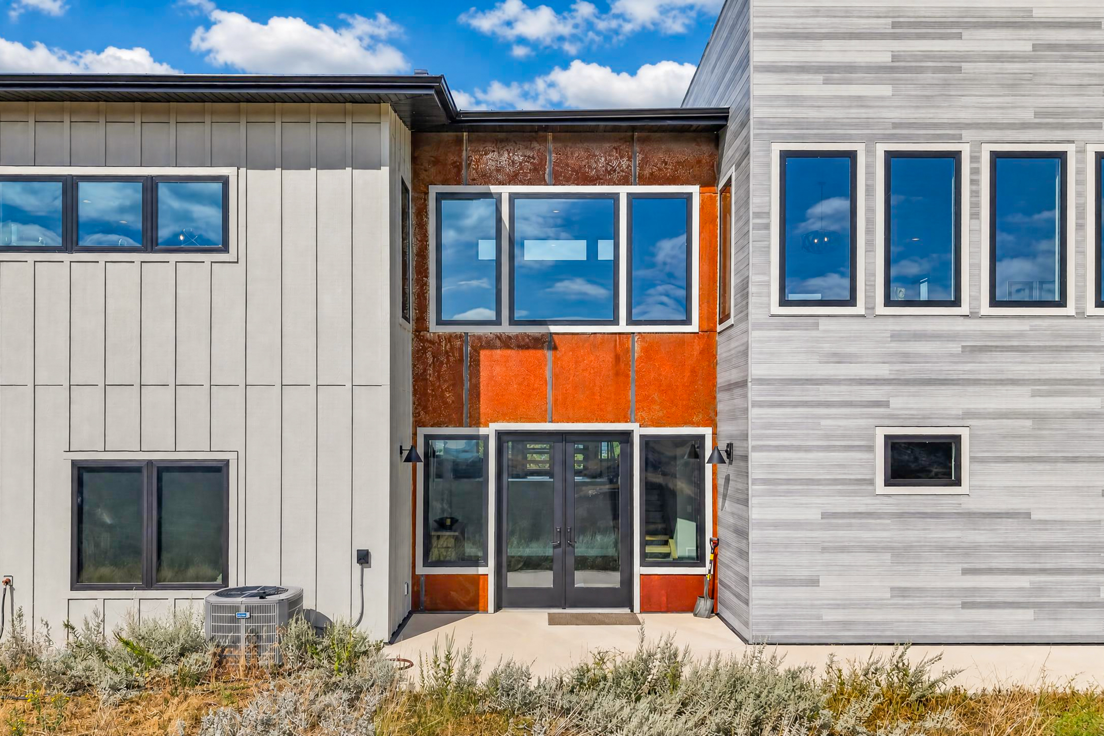 A close view of the entry shows weathered corten steel cladding framing dark double glass doors and tall windows above.