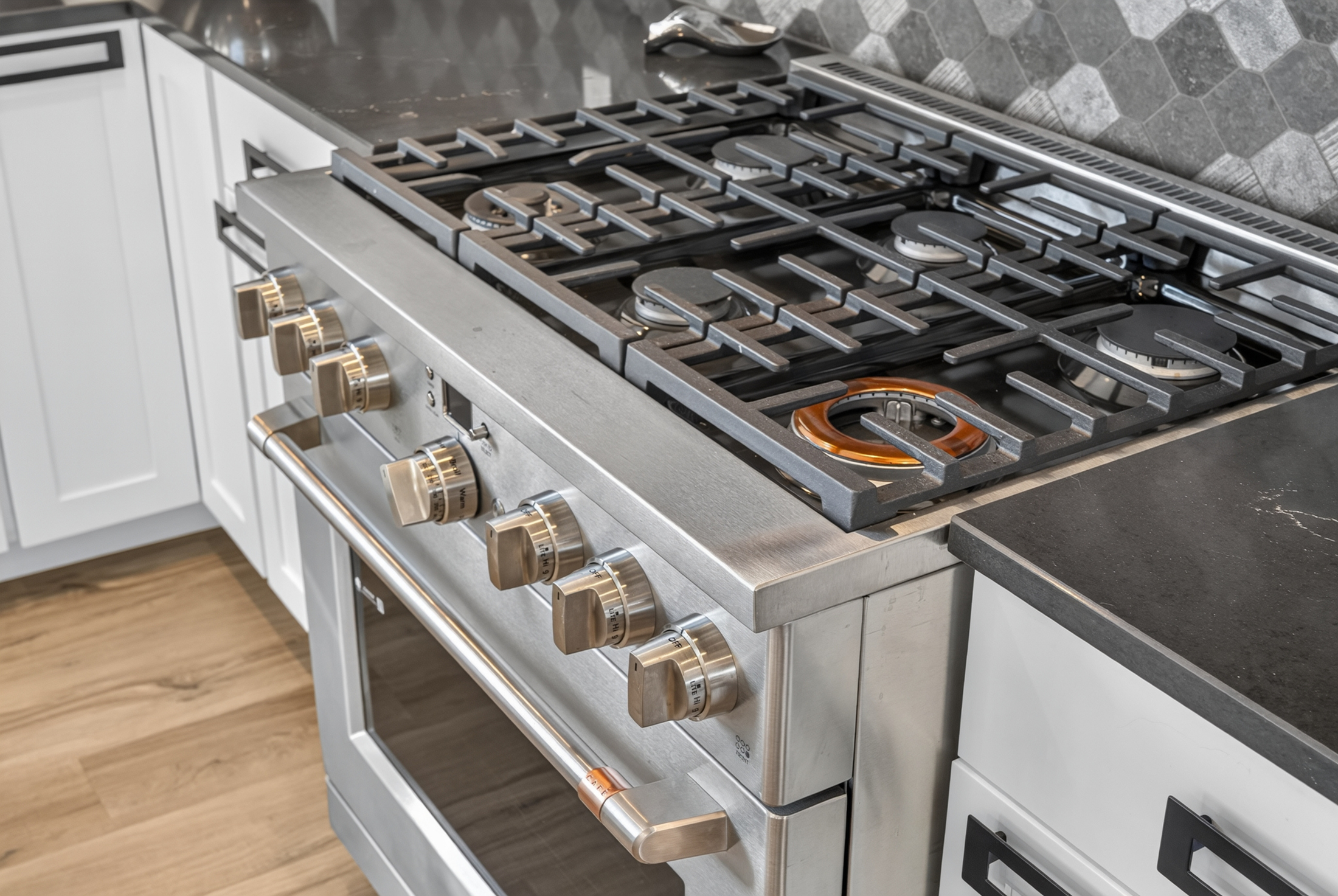A close view shows the gas range's burner grates and control knobs against the dark quartz counter and tile backsplash.