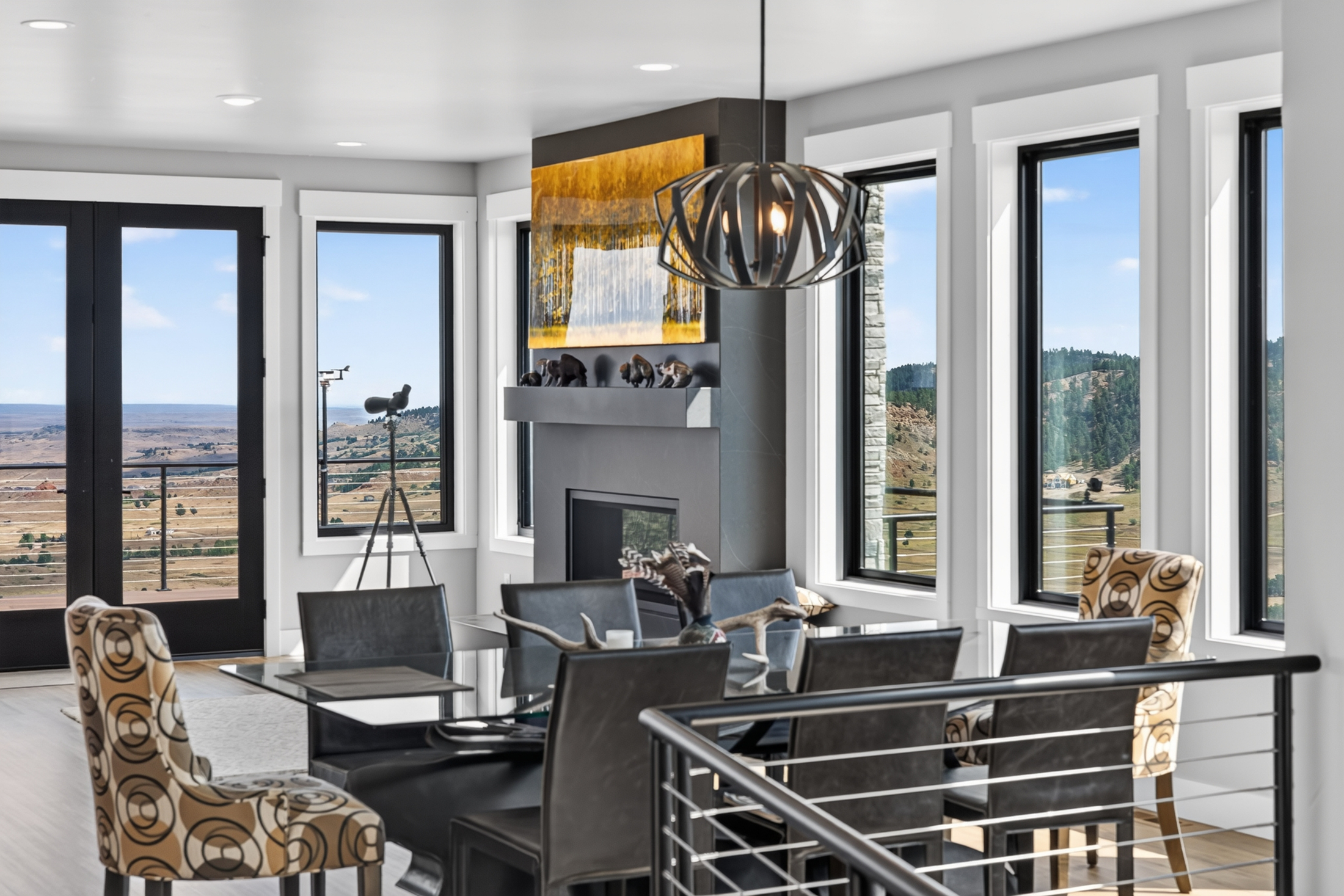 A gray stone fireplace with small bison figurines on the mantel sits between tall windows overlooking the hills.