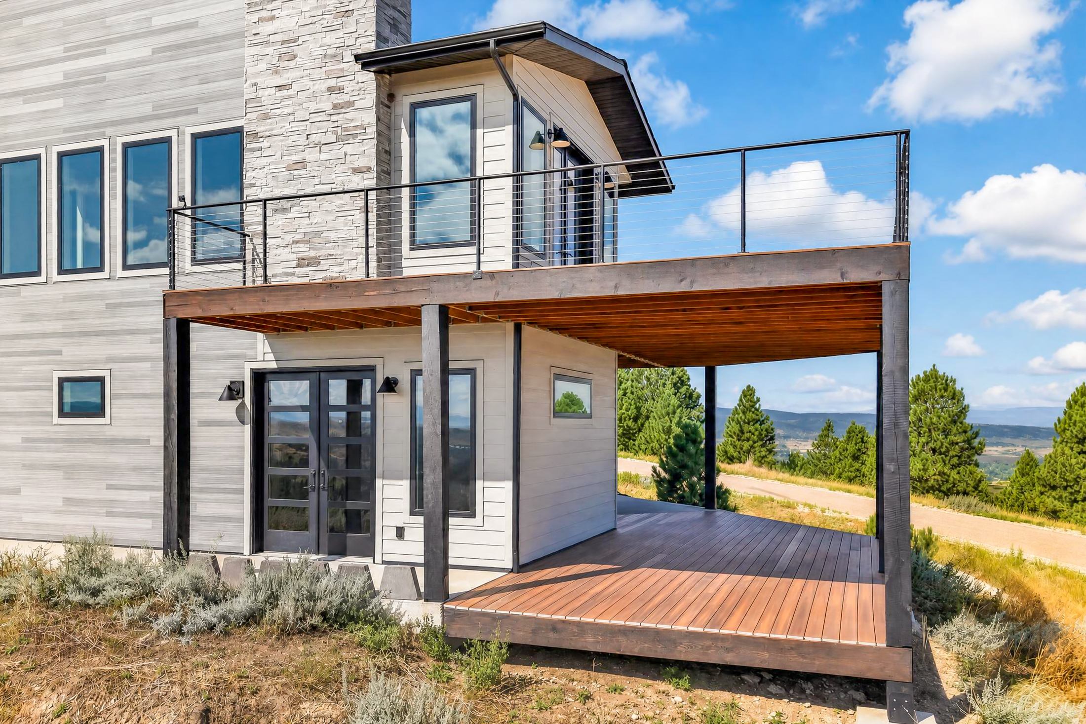 The covered lower deck at 2111 Vantage Circle sits beneath a cantilevered upper balcony with cable railing and a stone chimney above.