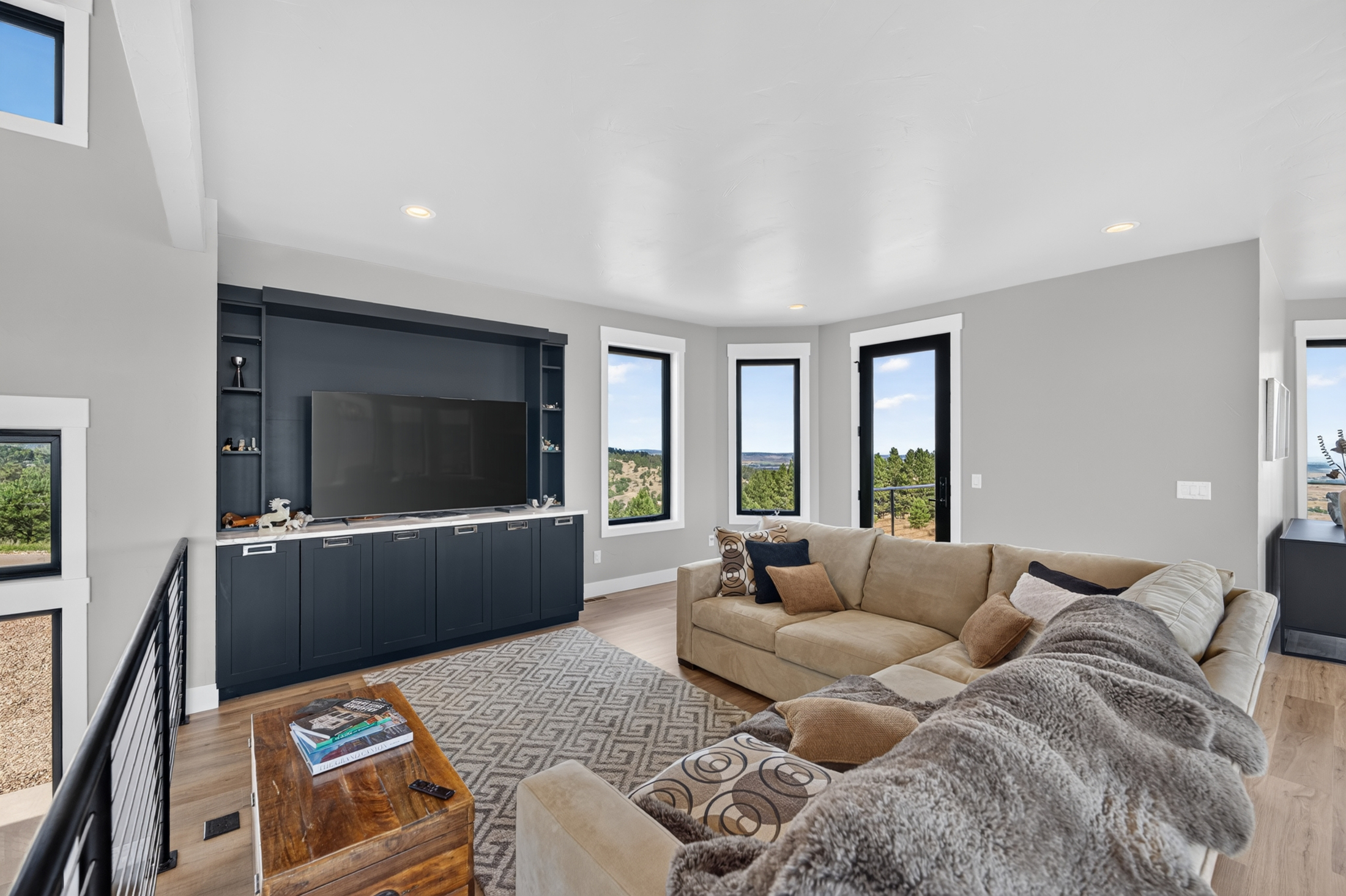 A large television sits in a navy built-in cabinet across from a sectional sofa with fur throws and patterned pillows.