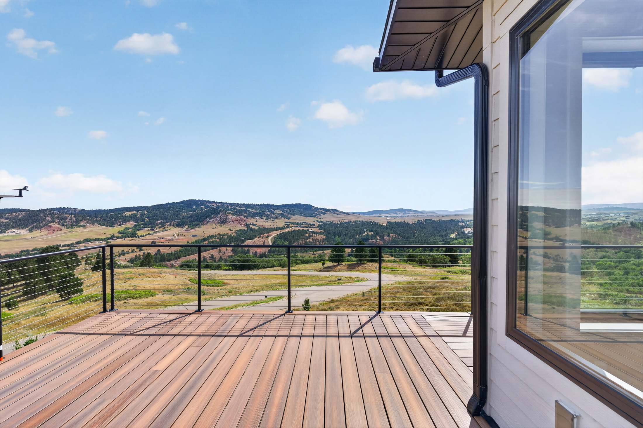 The corner of the deck frames a view of tree-covered hills and the valley road below the house.