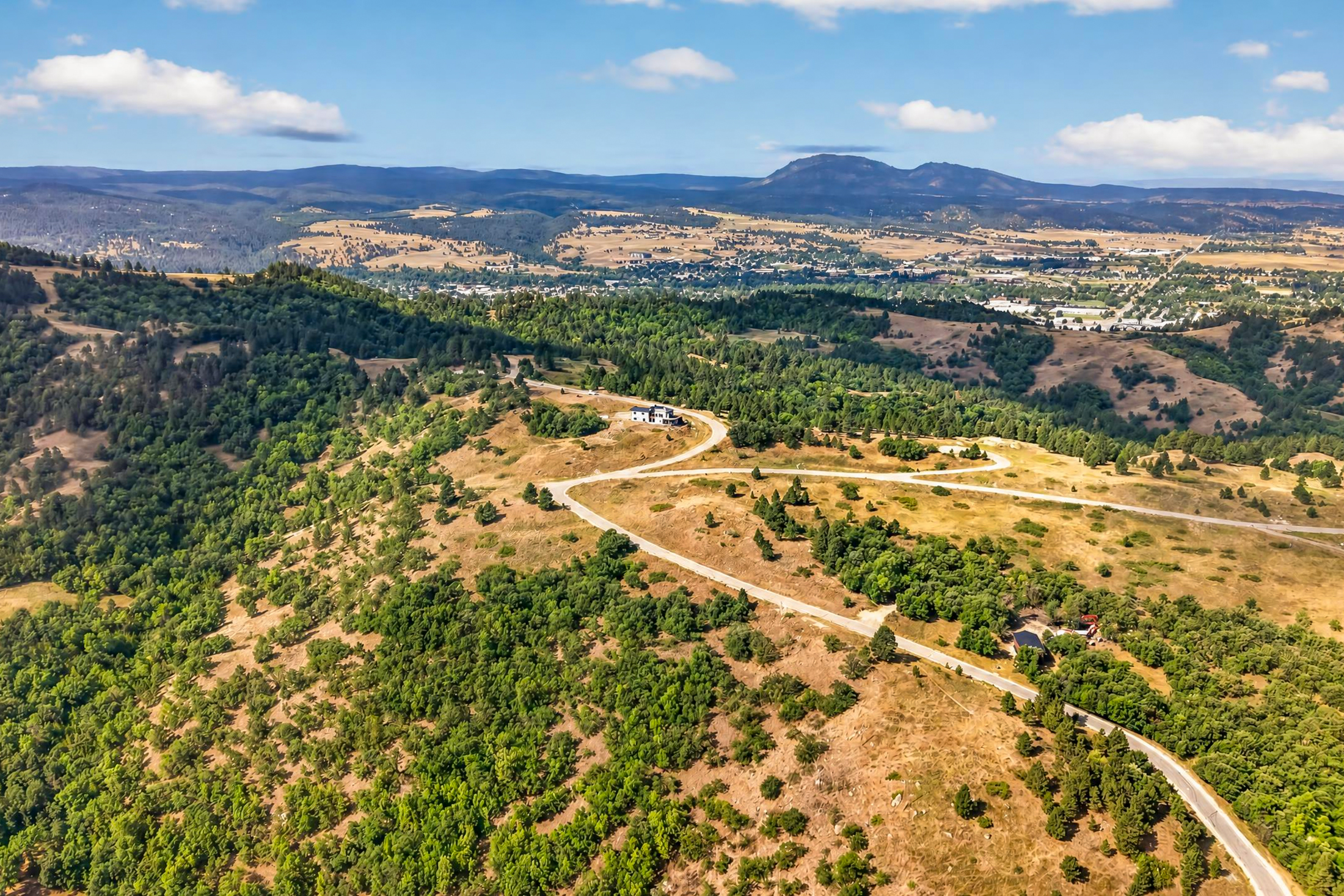 A wide aerial view shows a white house on a cleared hillside road