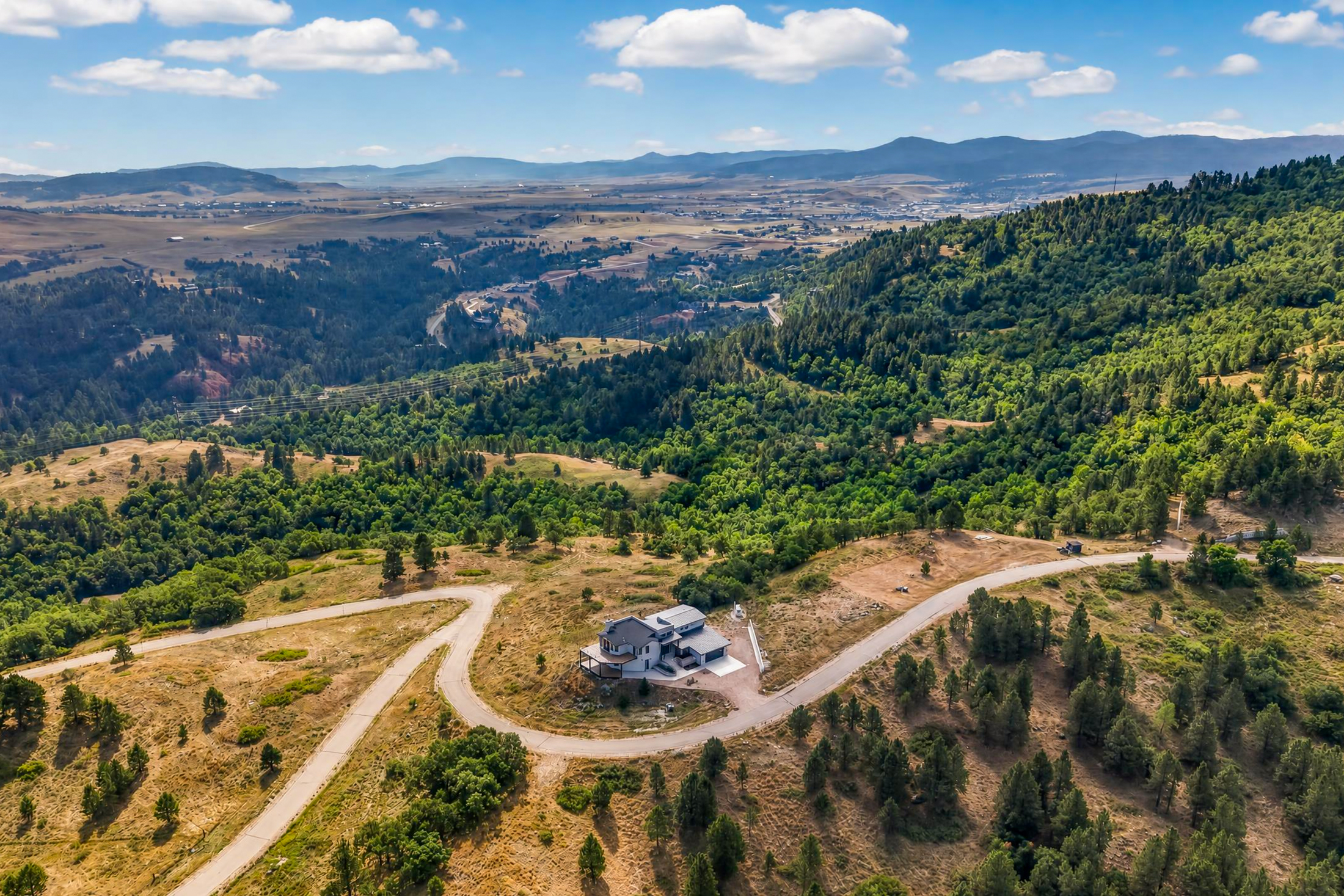 A wide aerial photograph places the house as a small structure within dense forest