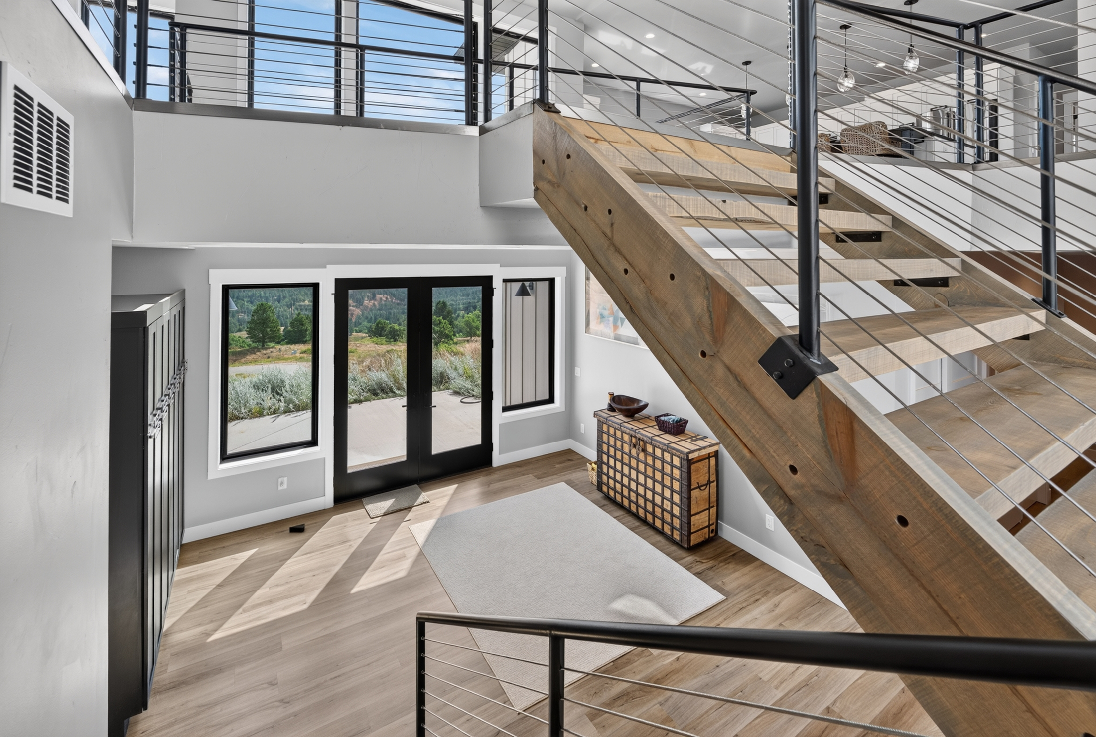 An entry hall with a glass door to the patio sits beneath an open wood and cable staircase.