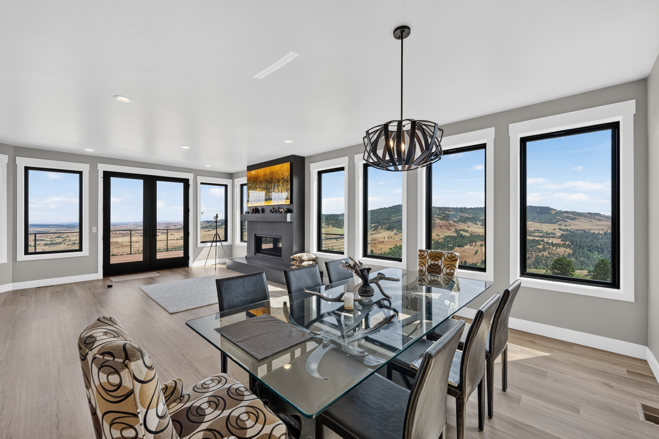 A glass-top dining table with an antler centerpiece is surrounded by leather and patterned chairs beneath a sculptural pendant light.