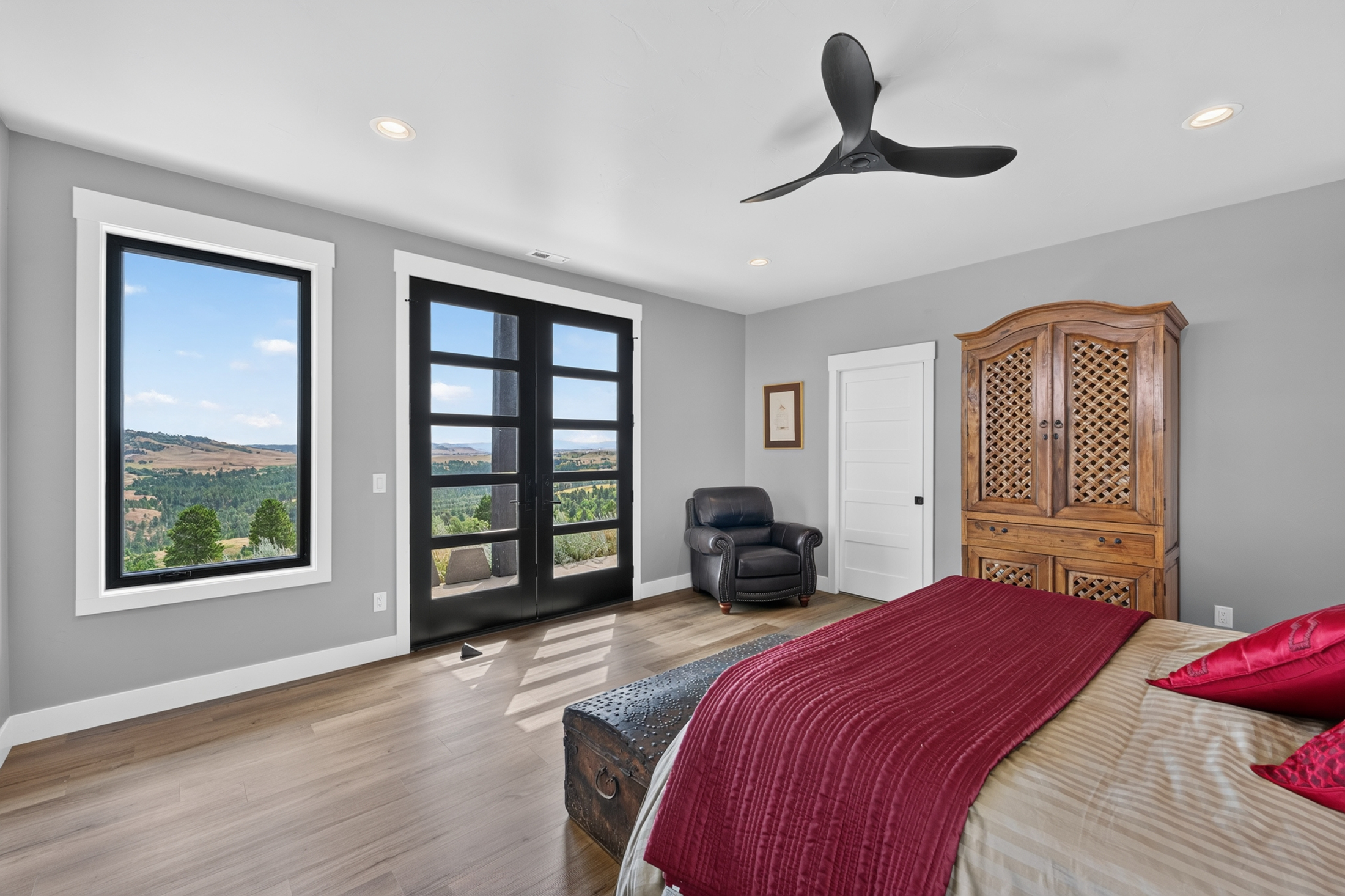 A guest bedroom opens through black-framed French doors onto a covered porch overlooking the Northern Black Hills.