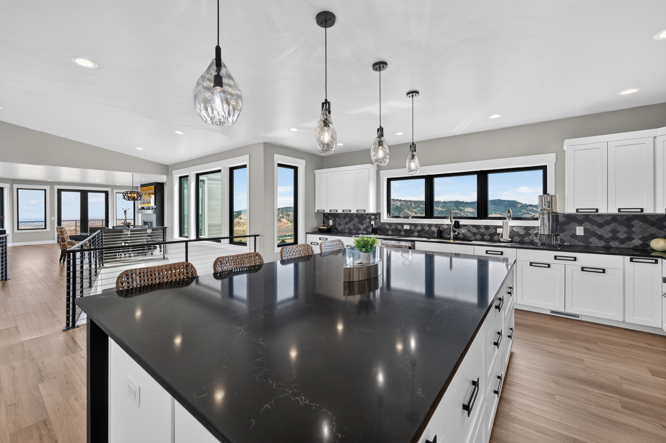 The kitchen island's dark countertop stretches toward a wall of windows, with the open living area visible down the hall.