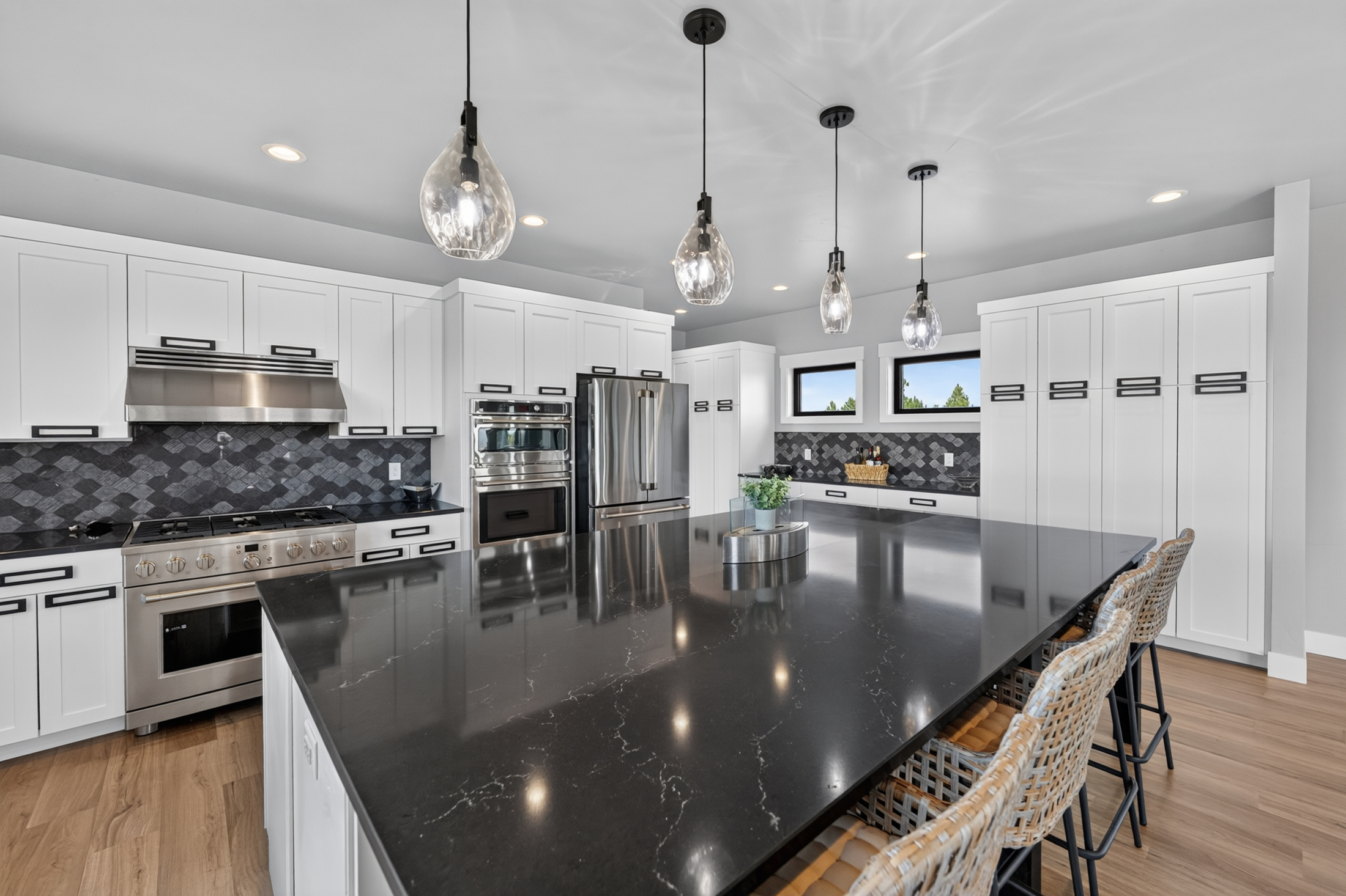 Three glass pendant lights hang above the black quartz island, with the gas range and ovens visible along the far wall.