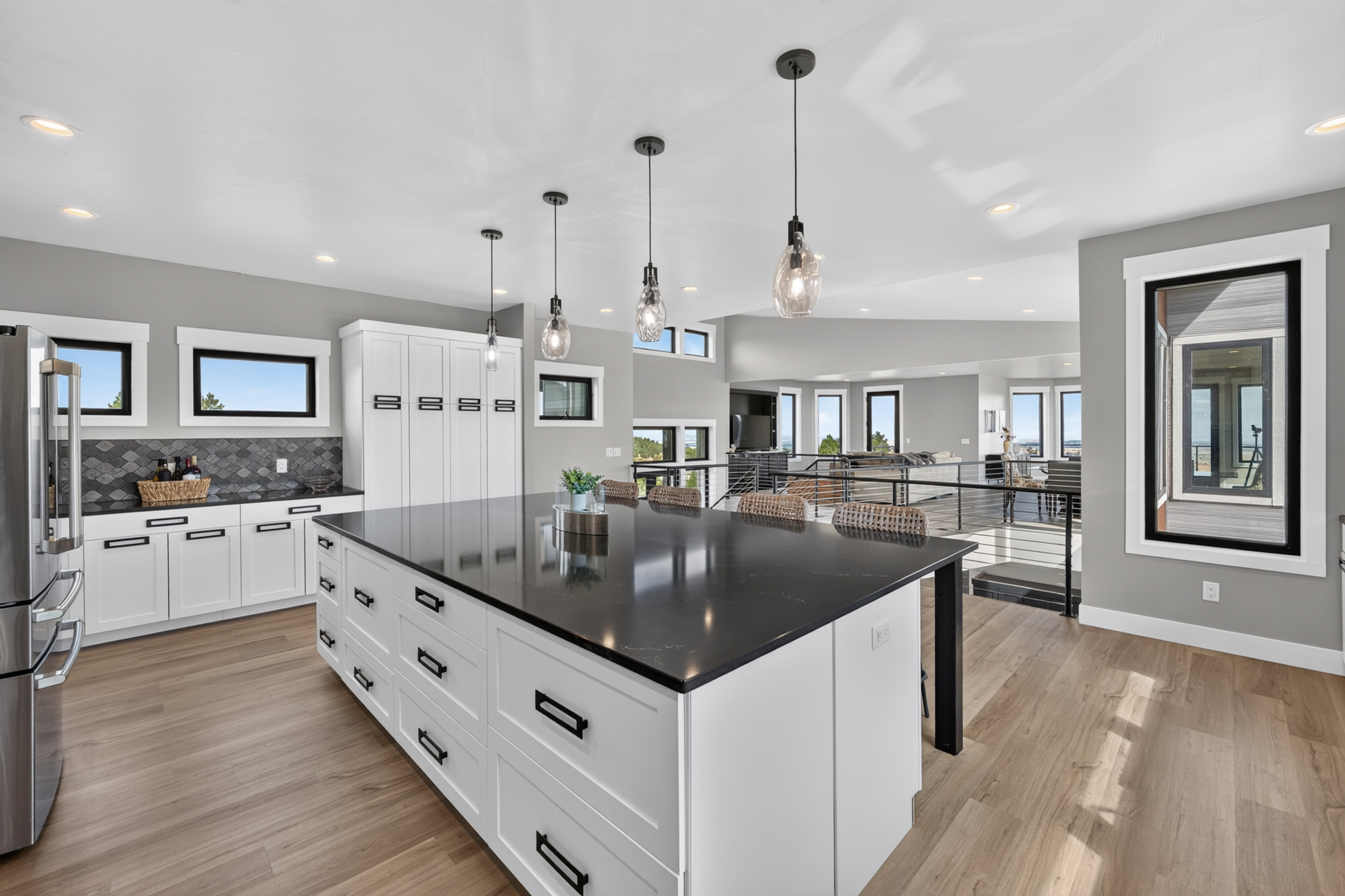 Tall pantry cabinets and a run of small windows overlook the staircase and living area beyond the kitchen island.