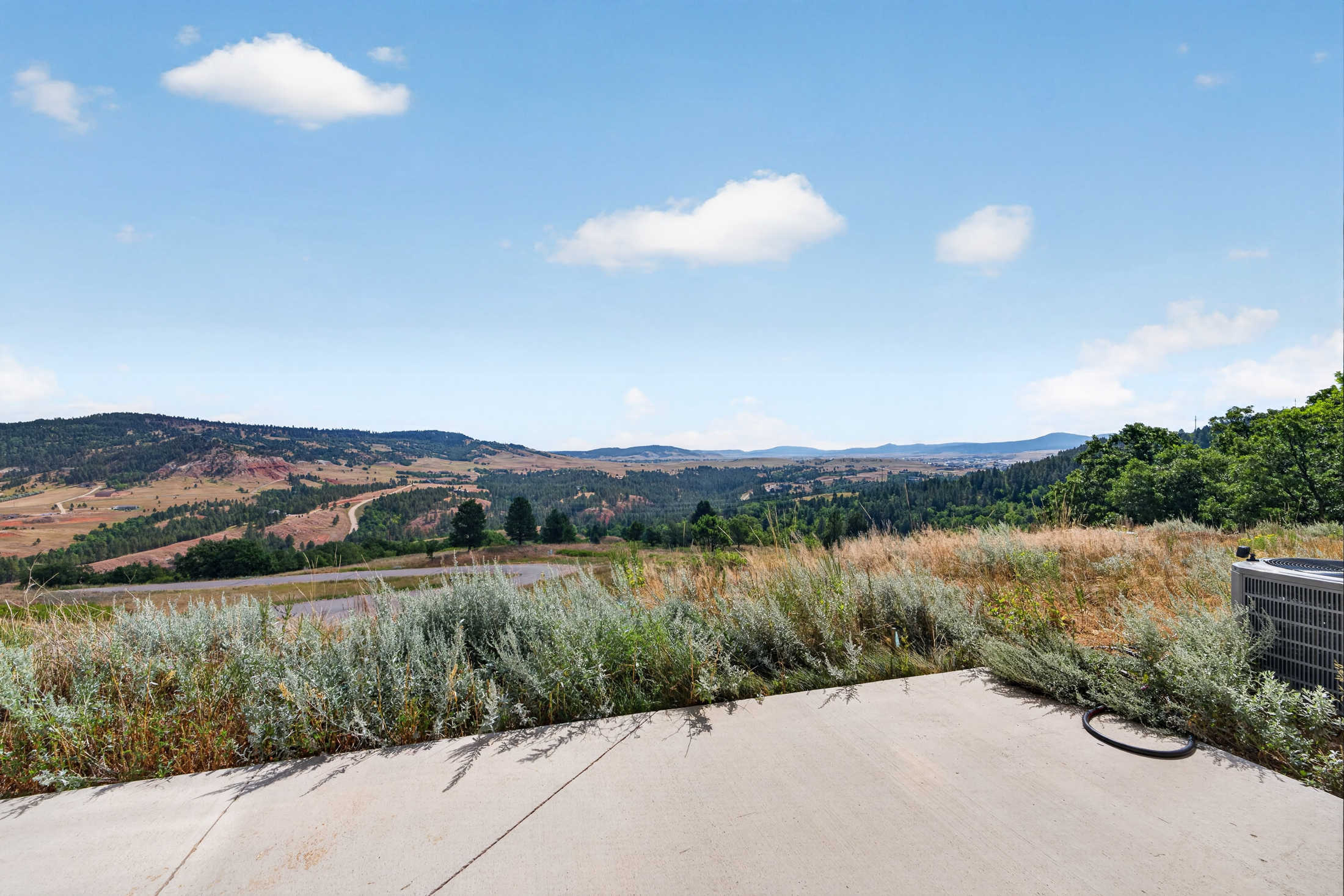 A concrete patio edge gives way to sagebrush and a long view across the valley toward distant mountains.