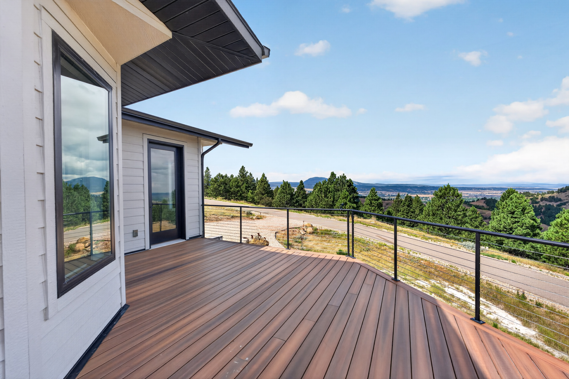A side deck with a black-framed door looks out over pine trees and low hills near 2111 Vantage Circle.