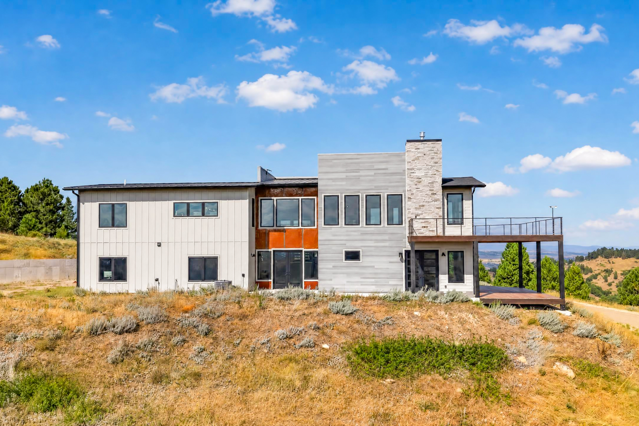 The side of the house shows a rust-colored corten steel panel between white board siding and gray horizontal siding