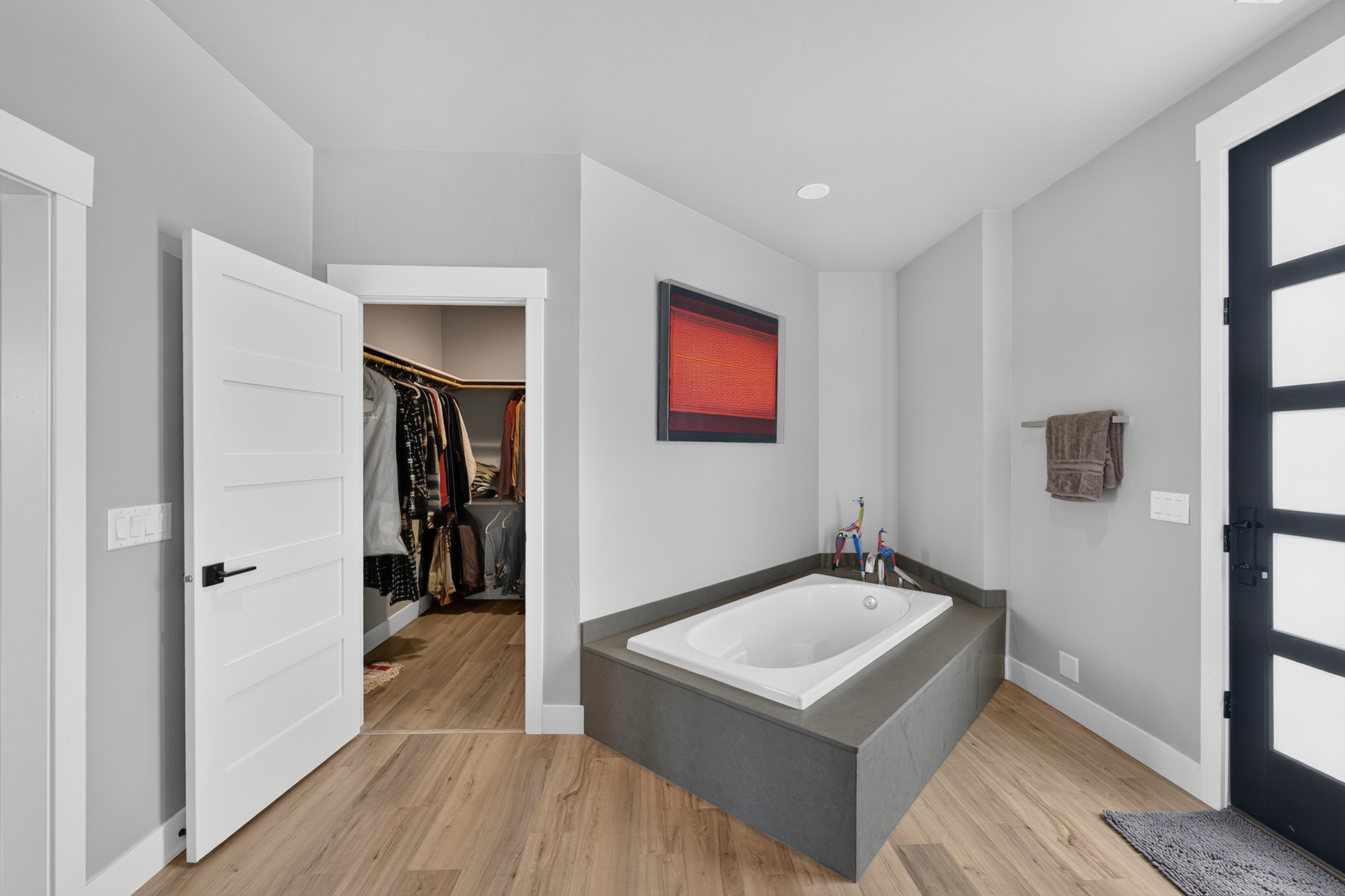 A freestanding-style soaking tub sits on a raised platform near an open closet door and a glass-paned entry door.