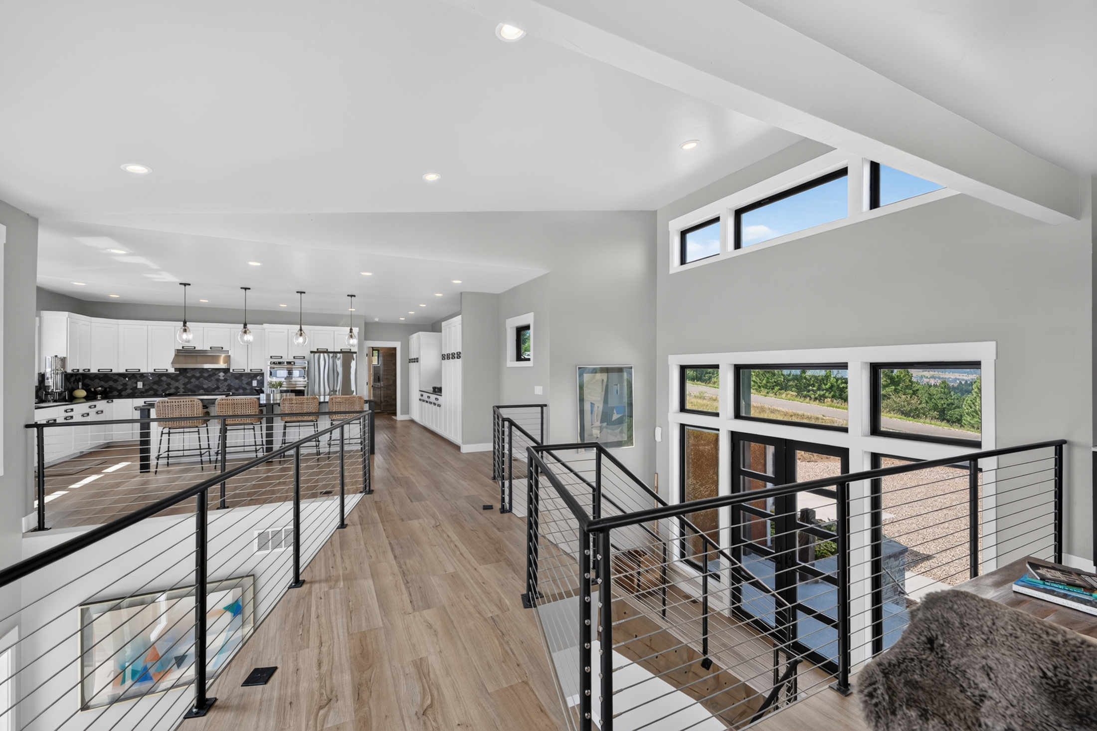 An upstairs hallway with wide-plank flooring overlooks the kitchen on one side and the glass entry doors on the other.