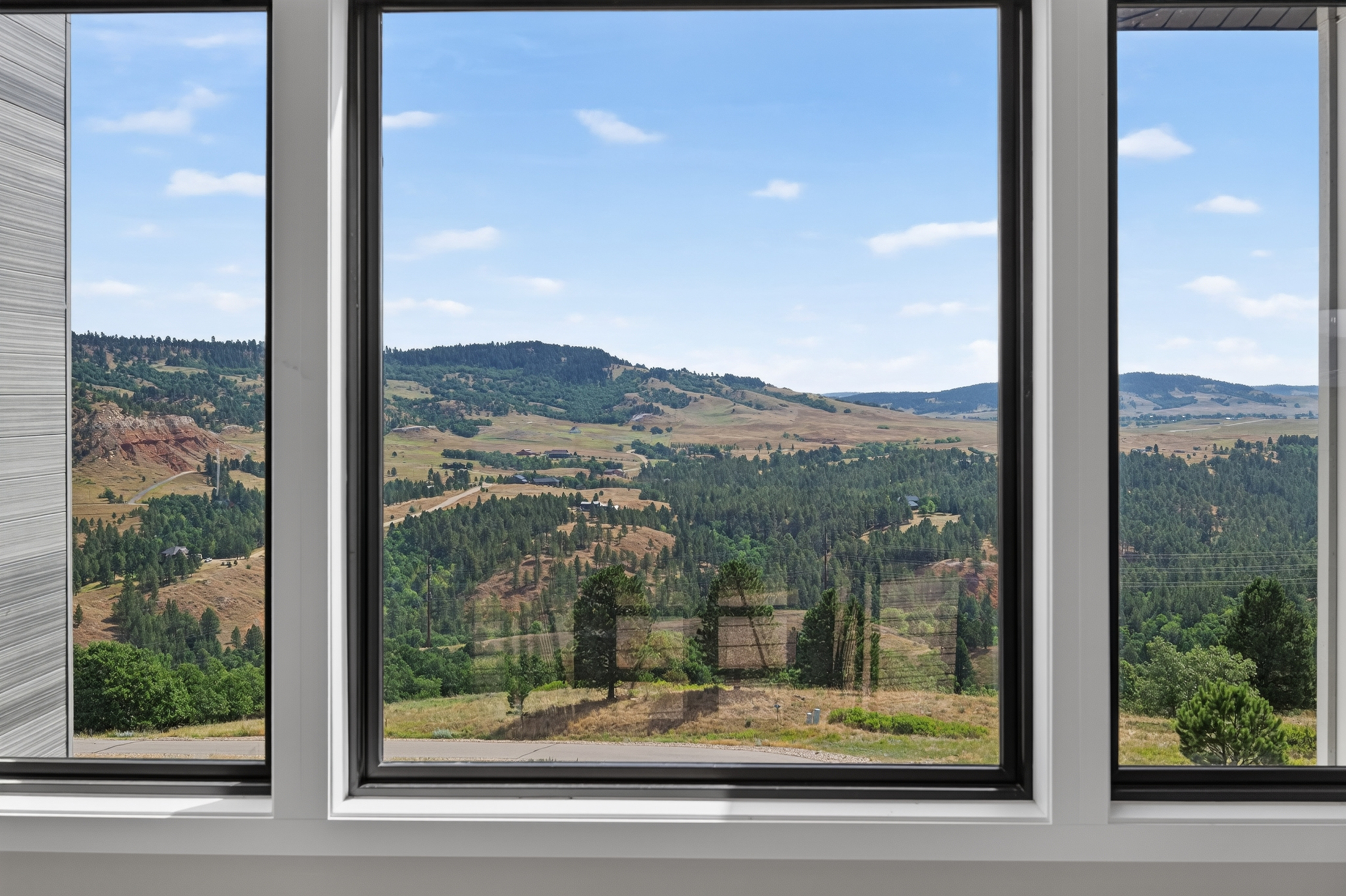 Three tall windows frame a forested valley with red rock outcrops and rolling farmland in the distance.